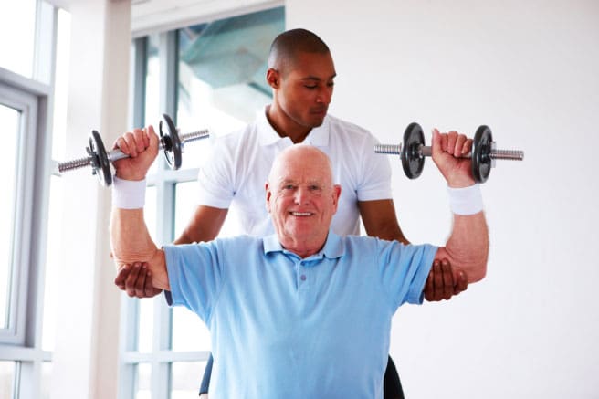 Caregiver Assisting Elderly Man Carrying Dumbells
