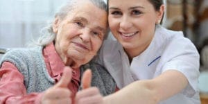 Caregiver and elderly woman giving a thumbs up or okay sign
