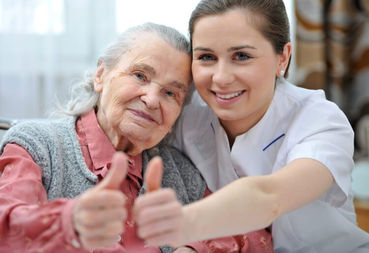 Caregiver and elderly woman giving a thumbs up or okay sign
